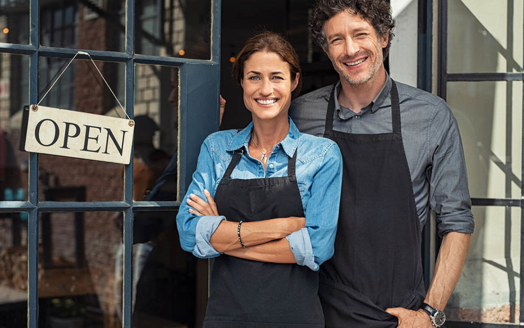 male and female coffee shop owners standing at the entrance to the coffee shop to great their customers after getting a business loan to expand their business