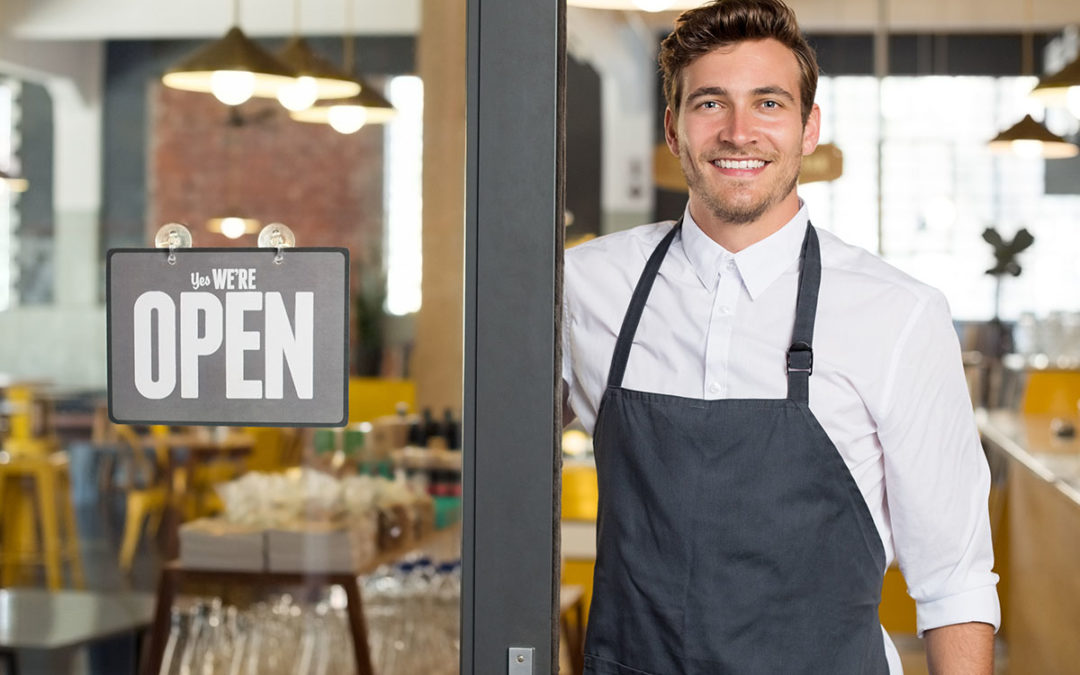 A coffee shop owner standing at the door to his coffee shop to show he is open for business